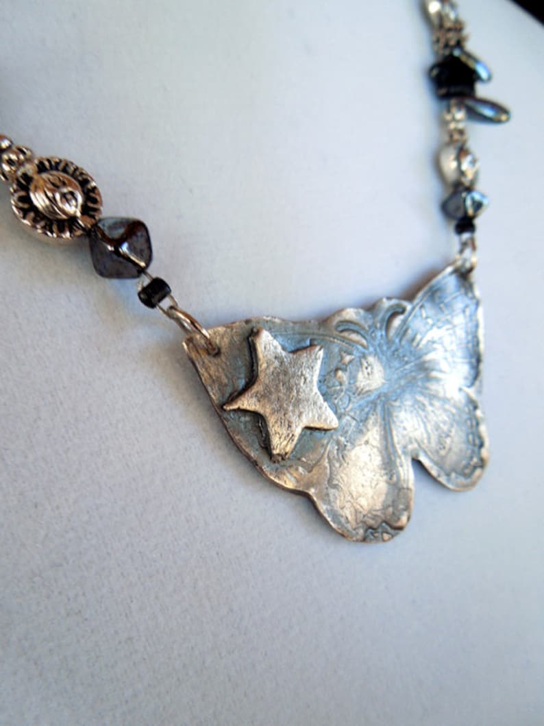 May include: A silver necklace with a butterfly pendant featuring a star design. The necklace is made with silver beads and black beads.