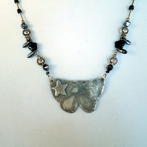 May include: A silver necklace with a butterfly pendant featuring a star. The necklace is made with black and silver beads.