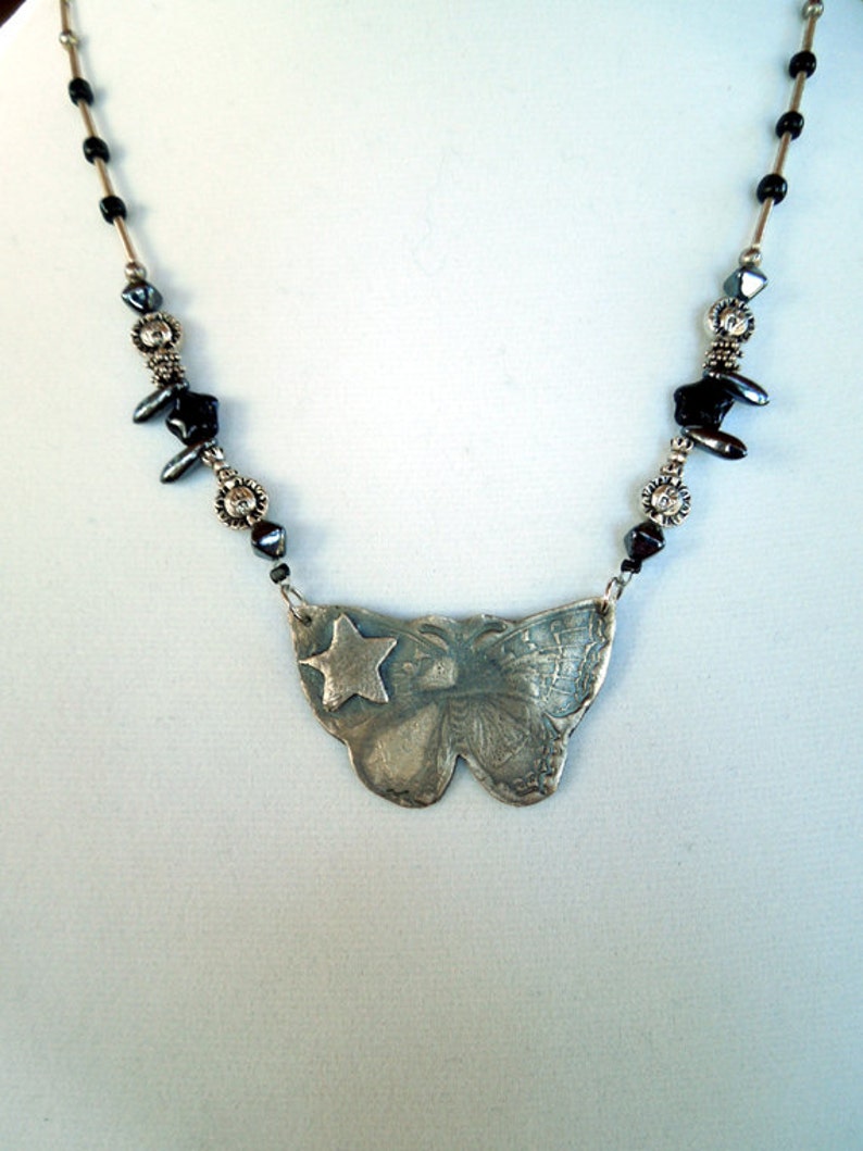 May include: A silver necklace with a butterfly pendant featuring a star. The necklace is made with black and silver beads.