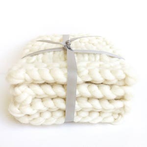 May include: A stack of four white knitted coasters tied together with a gray ribbon.
