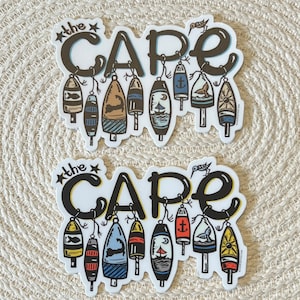 May include: Two stickers with the text "The Cape" in black and white lettering. Each sticker features a row of colorful nautical buoy designs with a small bird on top.