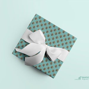 Puede incluir: Una caja de regalo azul verdosa con un lazo blanco. La caja está envuelta en papel con un patrón repetitivo de gatos de dibujos animados con sombreros. El texto "BLOCK21 prints" es visible en la esquina inferior derecha de la imagen.