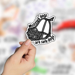 May include: A white sticker with a black and white illustration of a dog muzzle. The text "Muzzled dogs are safe dogs" is written on the sticker.