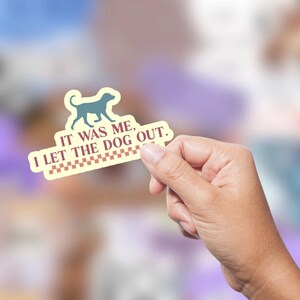 Op de afbeelding: Een gele sticker met een blauw silhouet van een hond die loopt. De sticker zegt "Het was ik, ik heb de hond eruit gelaten."