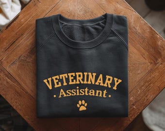 May include: A black sweatshirt with the text "VETERINARY Assistant." in yellow lettering and a paw print below.
