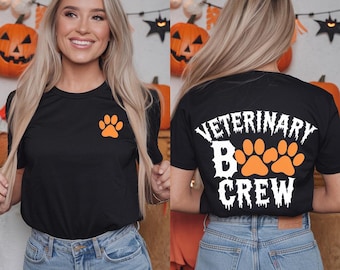 Peut inclure: T-shirt noir avec une empreinte de patte blanche sur le devant et "Veterinary Boo Crew" avec des empreintes de pattes orange au dos.