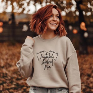 May include: A beige sweatshirt with a black graphic of two Australian Shepherd dog heads and the text "Australian Shepherd Mom".