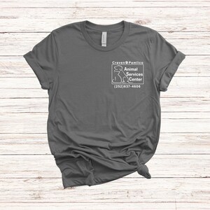 May include: A dark gray t-shirt with a white graphic of a dog and the text "Craven & Pamlico Animal Services Center (252) 637-4606"