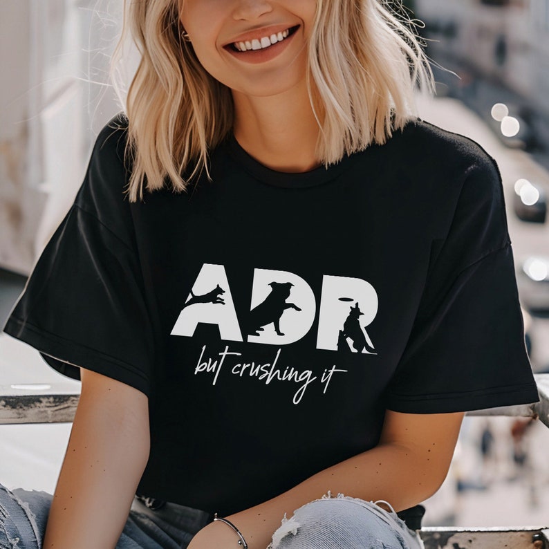 May include: A black t-shirt with a white graphic design that says "ADR but crushing it" with silhouettes of dogs playing fetch.