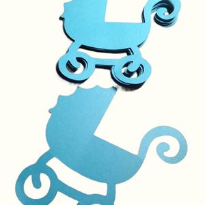 May include: A stack of multiple bright blue paper cutouts in the shape of a baby carriage. Each cutout features a scalloped hood, a curved handle, and four circular wheels. The paper has a subtle metallic sheen and a smooth, flat finish.