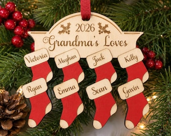 May include: A wooden Christmas ornament featuring the text 2026 and Grandma's Loves, with holly illustrations. Eight red wooden stockings are attached, each engraved with the names Victoria, Meghan, Jack, Kelly, Ryan, Emma, Sean, and Gavin.
