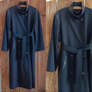 Può includere: Un cappotto lungo blu navy con un design doppiopetto, con cintura in vita e inserti in pelle sul colletto e sulle tasche. Il cappotto ha una silhouette classica e sartoriale.