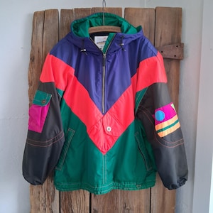 May include: A vintage color-blocked jacket with a hood. The jacket features a vibrant design with a purple upper section, a red chevron, and green lower section. It has a zip closure and pockets, with accents of pink and black.