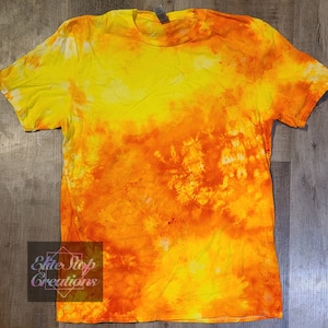 May include: A tie-dye t-shirt with a yellow and orange colour scheme. The shirt has a faded, tie-dye pattern with a gradient of yellow to orange.