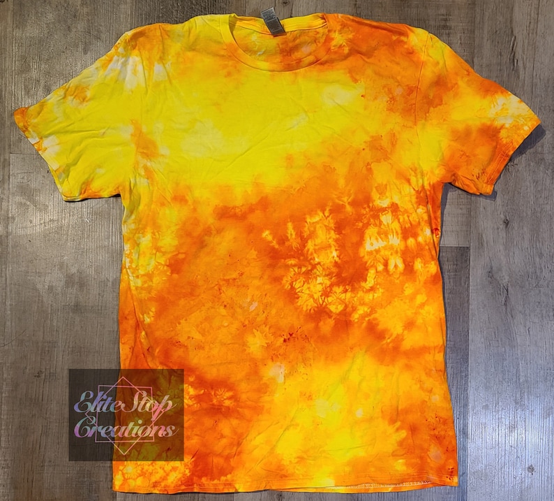 May include: A tie-dye t-shirt with a yellow and orange colour scheme. The shirt has a faded, tie-dye pattern with a gradient of yellow to orange.