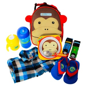 May include: A brown monkey lunch bag with the name "STELLAN" on it, a blue and yellow sippy cup, a blue and white plaid shirt, a red and yellow plate with a monkey face, a blue and red pair of flip flops, and two blue and yellow toy trains with the name "STELLAN" on them.