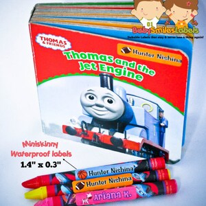 May include: A set of four colorful crayons with personalized waterproof labels. The labels feature a football, basketball, and a unicorn design. The labels are 1.4 inches by 0.3 inches. The labels are from BabySmilesLabels, which are durable and stay on.