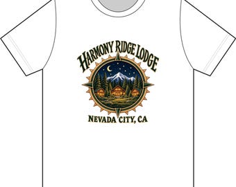 以下が含まれることがあります： 白い半袖Tシャツ。夜の山小屋、松の木、三日月、星が描かれた円形のグラフィックが中央にあります。コンパスのような枠の中に「Harmony Ridge Lodge」と「Nevada City, CA」という文字が記されています。