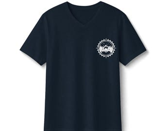 以下が含まれることがあります： 左胸に白いグラフィックが施されたネイビーブルーのVネックTシャツ。グラフィックはコンパス風の円形エンブレムで、山脈、松の木、そして山々の上の夜空に浮かぶ三日月が描かれています。