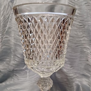 May include: A clear glass pedestal bowl with a diamond pattern. The bowl has a wide, flared rim and a tall, slender stem.