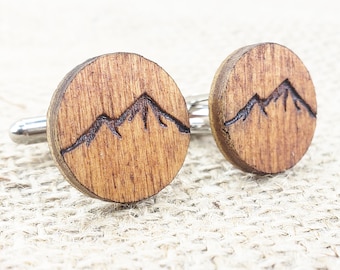 Puede incluir: Un par de gemelos de madera con un diseño de cordillera. Los gemelos son redondos y tienen un acabado de madera marrón oscuro.