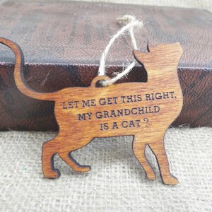 May include: Wooden cat ornament with the text "Let me get this right, my grandchild is a cat?"