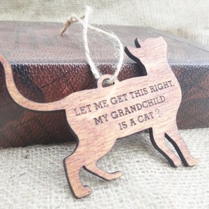May include: Wooden cat ornament with the text "Let me get this right. My grandchild is a cat?"