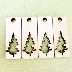 May include: Four wooden tags with a cutout of a pine tree. The tags are light brown and have a hole at the top for hanging.