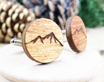 Puede incluir: Un par de gemelos de madera con un diseño de cordillera. Los gemelos son redondos y tienen un acabado de madera natural.