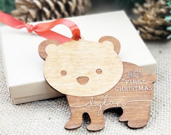 May include: Wooden bear Christmas ornament with the text "2021 First Christmas" and the name "dylan". The ornament has a light brown body and darker brown accents. A red ribbon is attached for hanging.