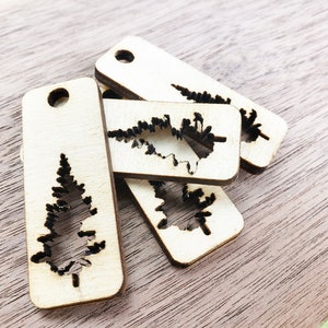 May include: Four wooden tags with a cutout of a pine tree. The tags are rectangular and have a hole at the top for hanging.