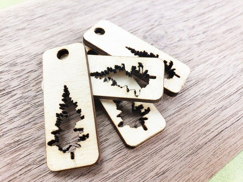 May include: Four wooden tags with a cutout of a pine tree. The tags are rectangular and have a hole at the top for hanging.