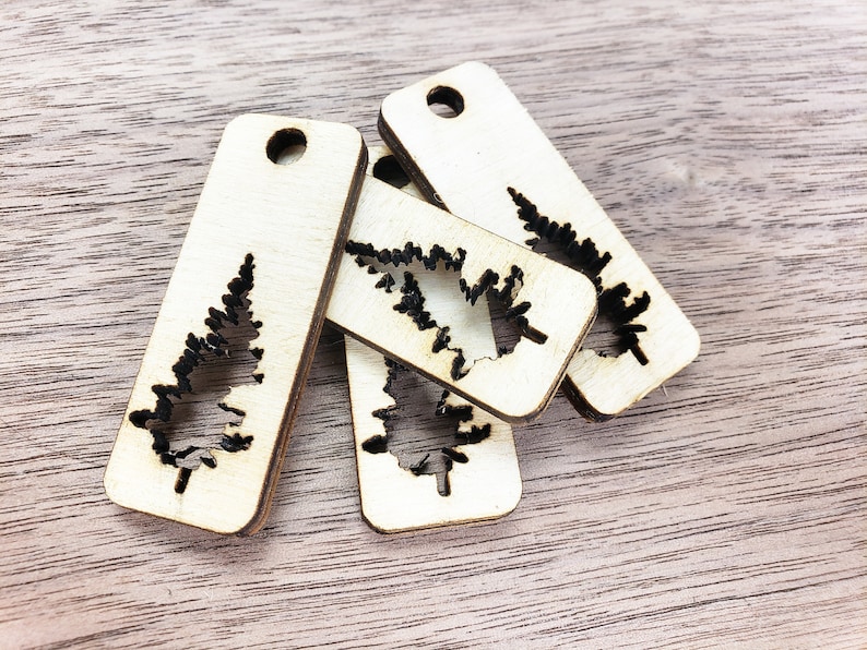 May include: Four unfinished wooden ornaments shaped like Christmas trees with a cutout design. The ornaments are stacked on top of each other.