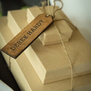 May include: A stack of three brown gift boxes tied with twine and a wooden gift tag that reads "Derek Hardy".