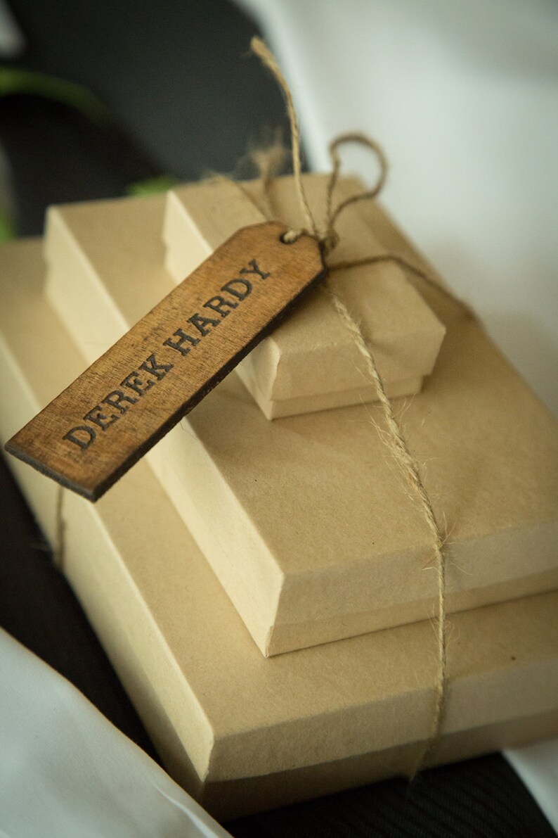 May include: A stack of three brown gift boxes tied with twine and a wooden gift tag that reads "Derek Hardy".
