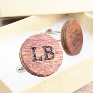 May include: A pair of wooden cufflinks with the initials "LB" engraved on each. The cufflinks are in a small box.