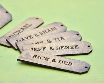 May include: Six wooden tags with names written on them. The tags are brown and have a natural wood finish. The names on the tags are "Michael", "Dave & Shari", "Tony & Tia", "Jeff & Renee", "Rick & Deb", and "Ora".