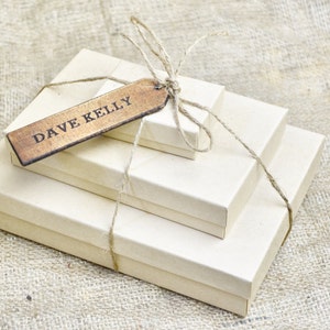 May include: Three brown cardboard boxes wrapped in twine with a wooden gift tag that reads "DAVE KELLY".
