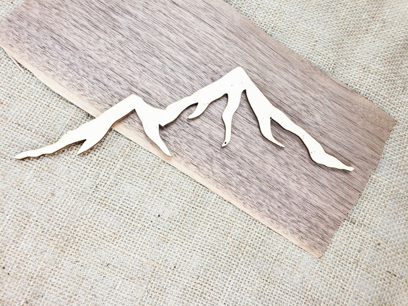 Op de afbeelding: Een wit houten silhouet van een berg op een bruin houten oppervlak.