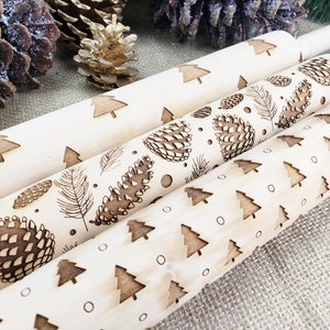 May include: Three wooden rolling pins with different Christmas-themed designs. The top rolling pin has a pattern of small Christmas trees. The middle rolling pin has a pattern of pine cones and feathers. The bottom rolling pin has a pattern of larger Christmas trees and small circles.