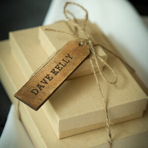 May include: Three brown gift boxes tied with twine and a wooden gift tag that says "DAVE KELLY".