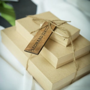 May include: Three brown cardboard boxes stacked on top of each other, tied together with twine. A wooden tag with the text "LEONARD JUATC" is attached to the boxes.