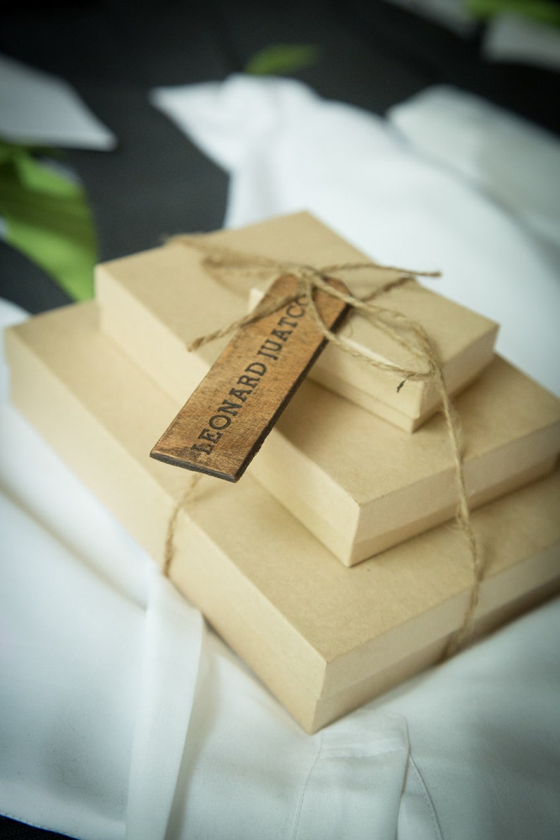 May include: Three brown cardboard boxes stacked on top of each other, tied together with twine. A wooden tag with the text "LEONARD JUATC" is attached to the boxes.