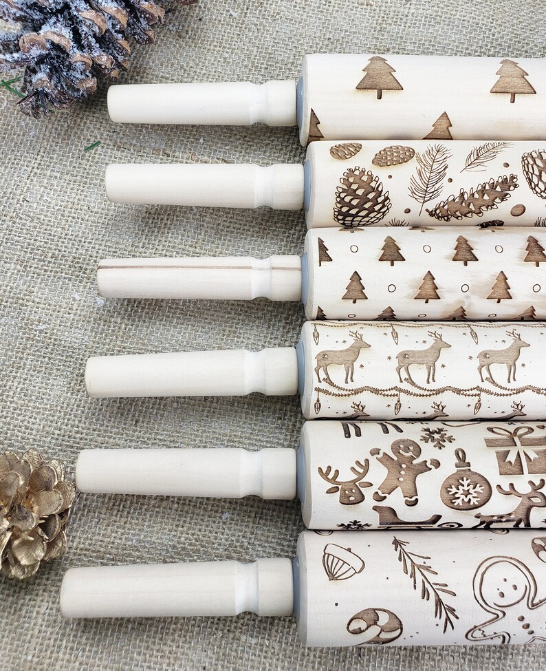 May include: Set of six wooden rolling pins with various Christmas-themed designs, including reindeer, pine trees, snowflakes, and ornaments. The rolling pins are all natural wood and have a light brown color.