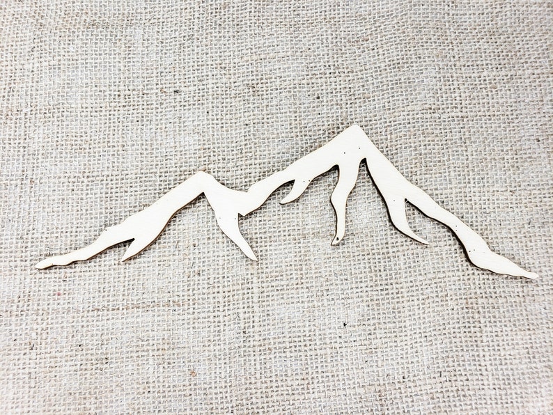 Op de afbeelding: Een wit houten berg silhouet uitsnijding, perfect voor knutselen of decoreren. De uitsnijding is op een jute achtergrond.