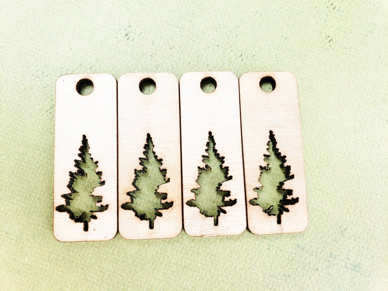 May include: Four wooden tags with a cutout of a pine tree. The tags are light brown and have a hole at the top for hanging.