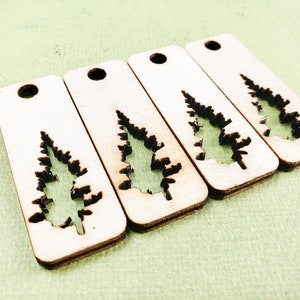 May include: Four wooden tags with a cutout of a pine tree. The tags are light brown and have a hole at the top for hanging.