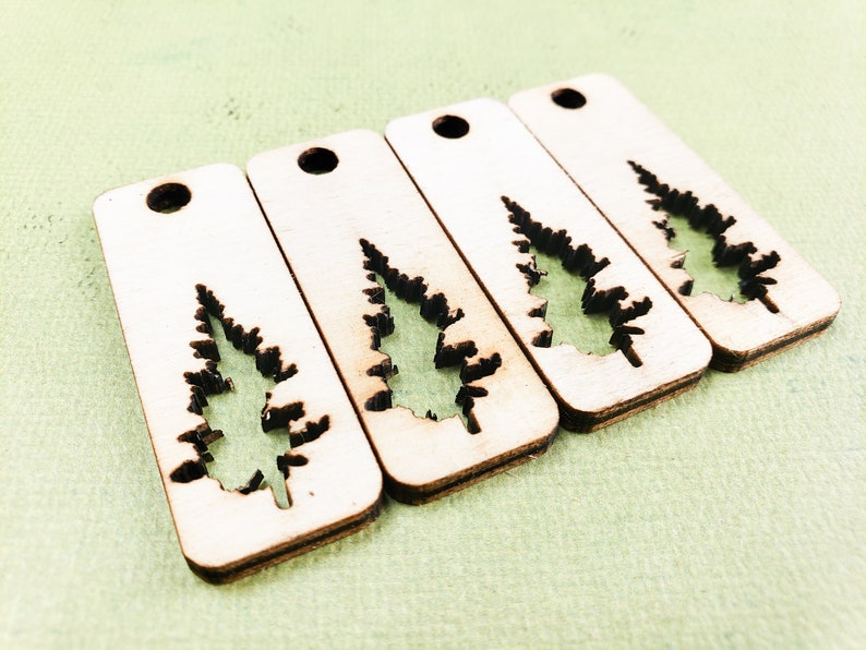 May include: Four wooden tags with a cutout of a pine tree. The tags are light brown and have a hole at the top for hanging.