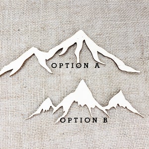 Op de afbeelding: Twee houten berg silhouetontwerpen, gelabeld "Optie A" en "Optie B". Beide ontwerpen tonen een gekartelde bergketen met toppen en valleien.