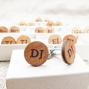 May include: A pair of wooden cufflinks with the initials "DJ" engraved on them. The cufflinks are in a white box and are surrounded by other cufflinks with different initials.